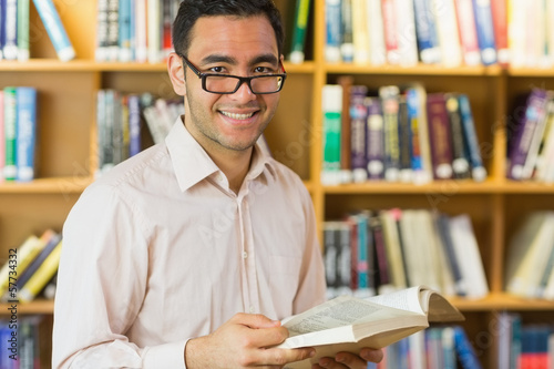 Photo: Smiling mature student reading book in library Smiling mature student reading book in library