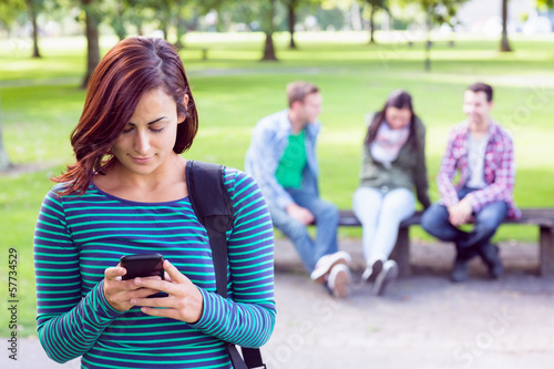 Photo: Female text messaging with blurred students sitting in park Female text messaging with blurred students sitting in park