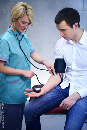 Photo: Female doctor checking young man blood pressure Female doctor checking young man blood pressure
