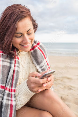 Photo: Smiling woman covered with blanket using cellphone at beach Smiling woman covered with blanket using cellphone at beach