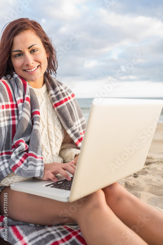 Photo: Woman covered with blanket using laptop at beach Woman covered with blanket using laptop at beach
