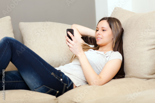 Photo: Woman lying on the couch and texting with her smartphone Woman lying on the couch and texting with her smartphone