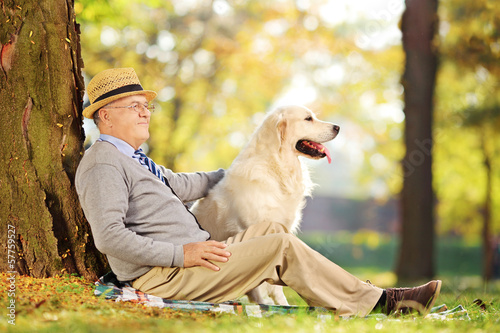 Photo: Senior gentleman and his dog sitting on ground in a park Senior gentleman and his dog sitting on ground in a park