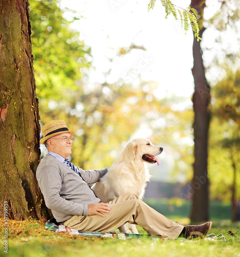 Photo: Senior gentleman and his dog sitting on ground in a park Senior gentleman and his dog sitting on ground in a park
