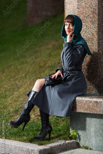 Photo: Sad young woman in classic coat sitting at the wall Sad young woman in classic coat sitting at the wall