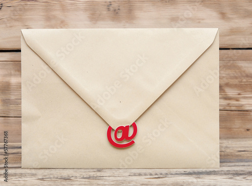 Photo: E-mail symbol and blank brown envelope on old wooden background E-mail symbol and blank brown envelope on old wooden background