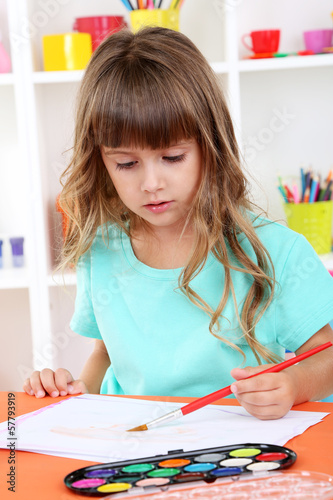 Photo: Little girl draws sitting at table in room on shelves Little girl draws sitting at table in room on shelves