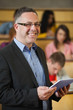 Foto: Lecturer holding tablet pc in front of class in lecture hall smiling at camera Lecturer holding tablet pc in front of class in lecture hall smiling at camera