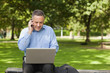 Photo : Cheerful professor talking on phone while sitting on bench using laptop on campus Cheerful professor talking on phone while sitting on bench using laptop on campus