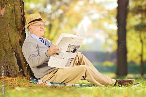 Photo: Smiling senior gentleman seated reading a newspaper in a park Smiling senior gentleman seated reading a newspaper in a park