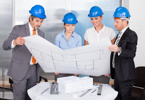 Photo: Architects Wearing Blue Hardhat Looking At Blueprint Architects Wearing Blue Hardhat Looking At Blueprint