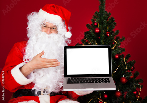 Photo: Portrait of a happy santa holding laptop Portrait of a happy santa holding laptop