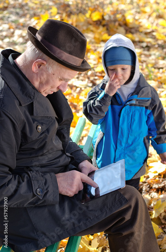 Photo: Grandfather using a tablet watched by his grandson Grandfather using a tablet watched by his grandson