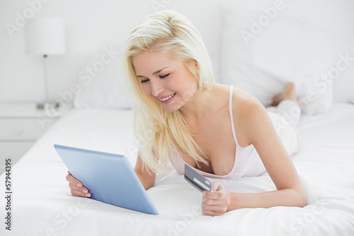 Photo: Casual young blond doing online shopping in bed Casual young blond doing online shopping in bed