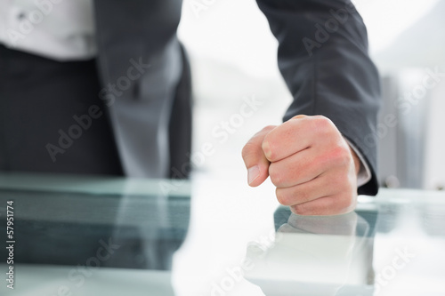 Photo: Mid section of businessman with clenched fist on office desk Mid section of businessman with clenched fist on office desk