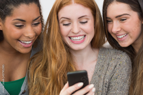 Photo: Close up of cheerful friends looking at mobile phone together Close up of cheerful friends looking at mobile phone together