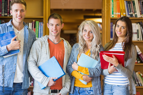 Photo: Students with folders standing against bookshelf in library Students with folders standing against bookshelf in library
