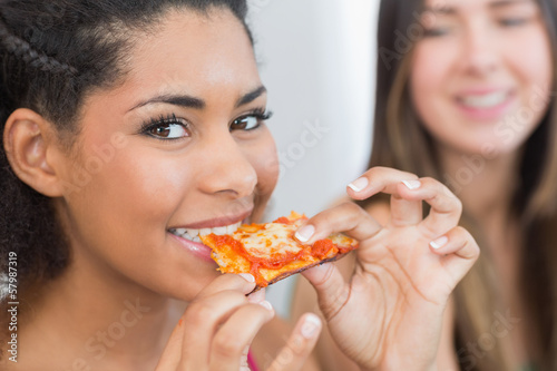Photo: Close up portrait of a female eating pizza with blurred friend Close up portrait of a female eating pizza with blurred friend