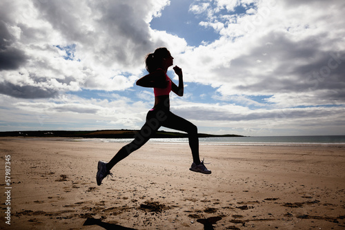 Photo: Full length of silhouette healthy woman jogging on beach Full length of silhouette healthy woman jogging on beach
