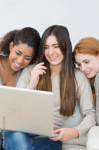 Photo: Cheerful female friends using laptop together on sofa Cheerful female friends using laptop together on sofa