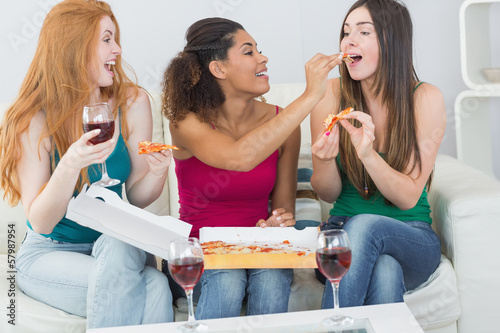 Photo: Happy female friends eating pizza with wine at home Happy female friends eating pizza with wine at home