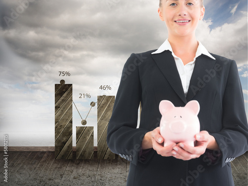 Photo: Composite image of businesswoman holding piggy bank Composite image of businesswoman holding piggy bank
