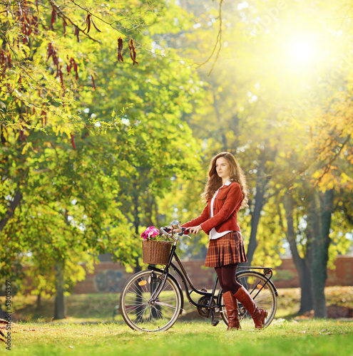 Photo: Young female with bicycle relaxing in a park on a sunny day Young female with bicycle relaxing in a park on a sunny day