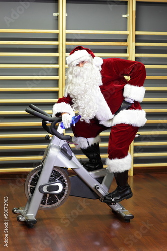 Photo: active Santa Claus break in training on exercise bike active Santa Claus break in training on exercise bike