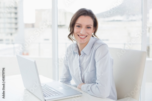 Photo: Smiling young businesswoman with laptop in office Smiling young businesswoman with laptop in office