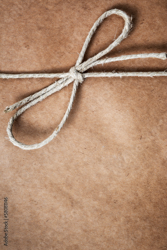 Photo: String tied in a bow, over brown package paper String tied in a bow, over brown package paper