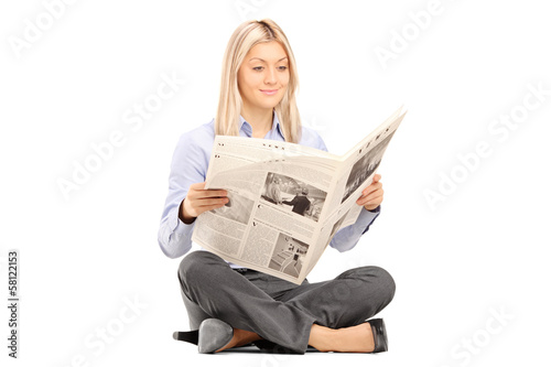 Photo: Young smiling woman sittong on a floor and reading a newspaper Young smiling woman sittong on a floor and reading a newspaper