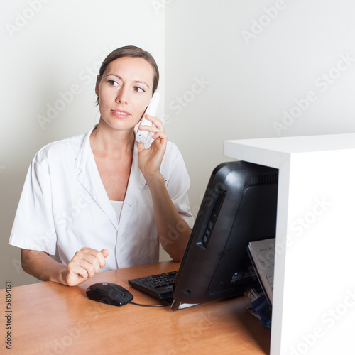 Photo: Medical receptionist on phone in front of computer Medical receptionist on phone in front of computer