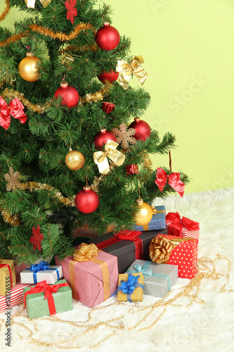 Photo: Decorated Christmas tree with gifts on green wall background Decorated Christmas tree with gifts on green wall background