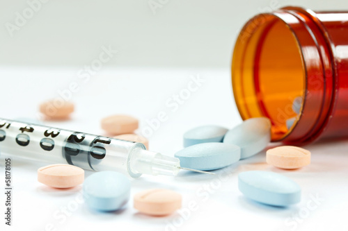 Photo: Pills spilling out of pill bottle and Syringe isolated on white Pills spilling out of pill bottle and Syringe isolated on white