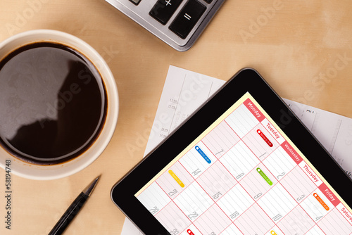 Photo: Tablet pc showing calendar on screen with a cup of coffee on a d Tablet pc showing calendar on screen with a cup of coffee on a d