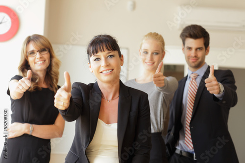 Photo: Happy business team showing thumbs up in the office Happy business team showing thumbs up in the office
