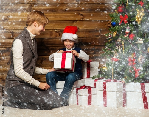 Photo: Mother and her lIttle boy in Santa hat opening gift box Mother and her lIttle boy in Santa hat opening gift box