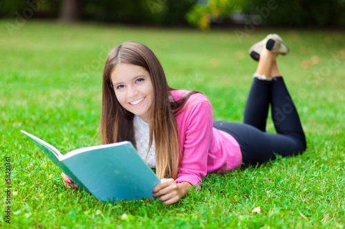 Photo: Female student reading a book lying on the grass Female student reading a book lying on the grass