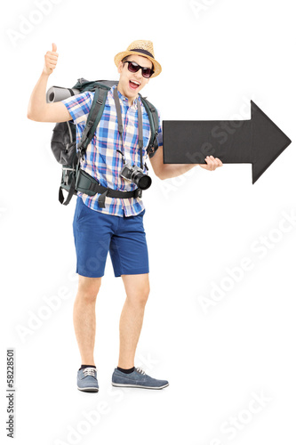 Photo: Hiker with backpack holding a big arrow and giving thumb up Hiker with backpack holding a big arrow and giving thumb up