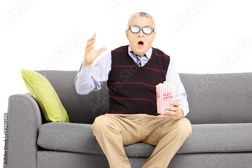 Photo: Shocked senior man sitting on a sofa and watching movie Shocked senior man sitting on a sofa and watching movie