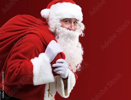 Photo: Portrait of Santa Claus carrying huge red sack with presents Portrait of Santa Claus carrying huge red sack with presents
