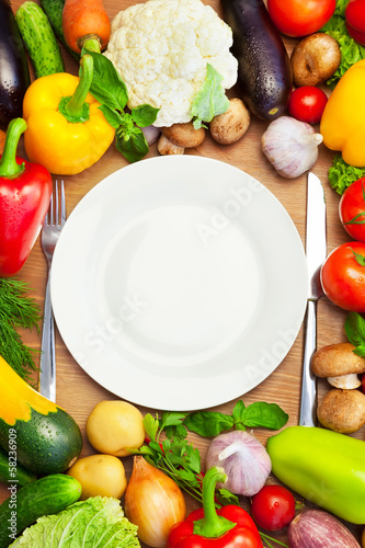 Photo: Organic Vegetables Around White Plate with Knife and Fork Organic Vegetables Around White Plate with Knife and Fork