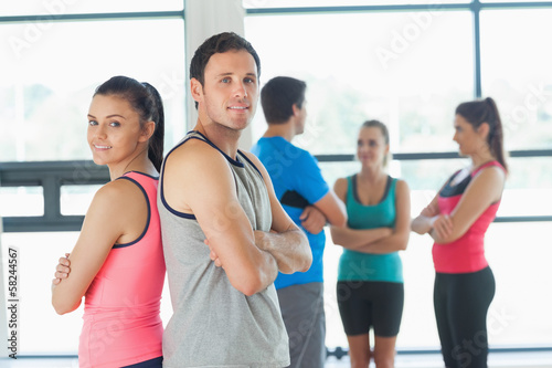 Photo: Fit couple with friends standing in background in exercise room Fit couple with friends standing in background in exercise room