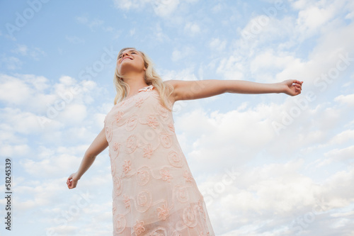 Photo: Young woman in summer dress stretching arms against sky Young woman in summer dress stretching arms against sky