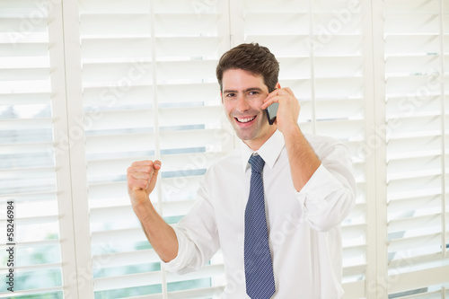 Photo: Smiling businessman using mobile phone while clenching fist Smiling businessman using mobile phone while clenching fist