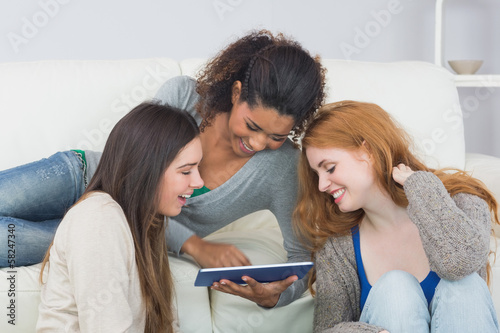 Photo: Female friends using digital tablet together at home Female friends using digital tablet together at home