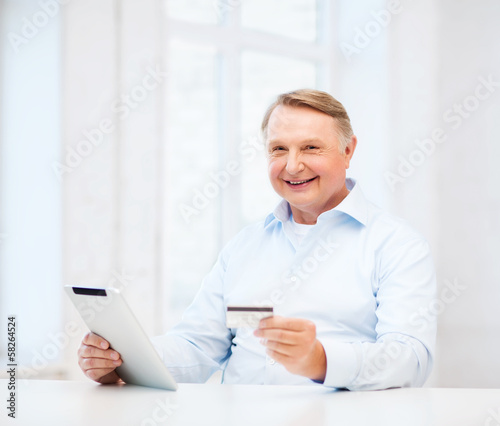 Photo: old man with tablet pc and credit card at home old man with tablet pc and credit card at home