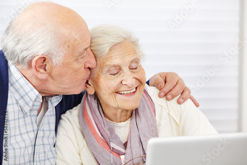 Photo: Senior küsst seine Frau am Computer auf die Wange Senior küsst seine Frau am Computer auf die Wange