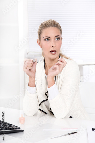 Photo: Junge blonde Frau lackiert sich im Büro die Nägel Junge blonde Frau lackiert sich im Büro die Nägel