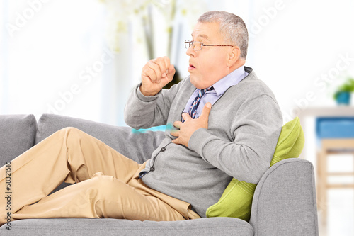 Photo: Mature man seated on a sofa coughing at home Mature man seated on a sofa coughing at home